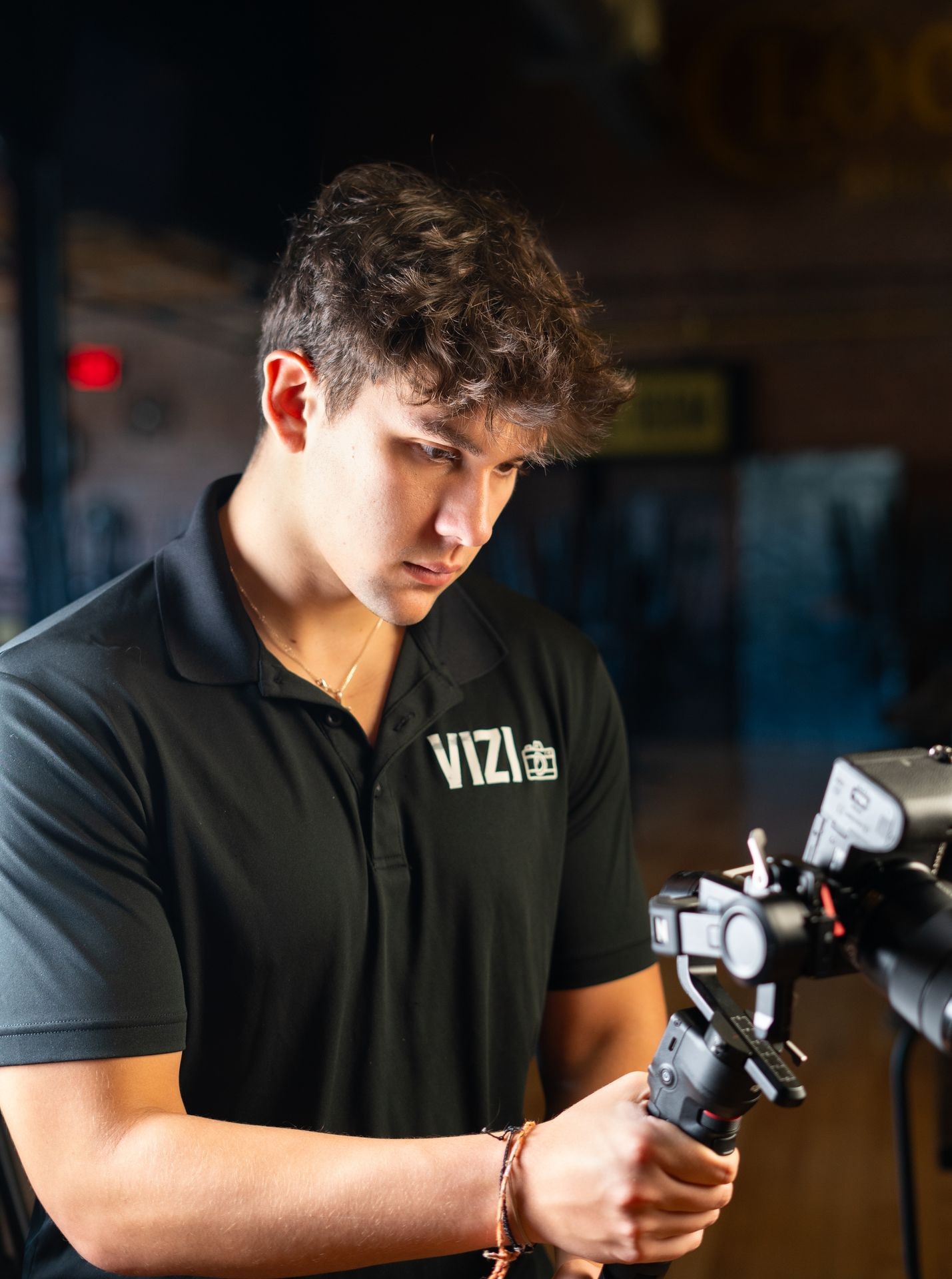 Person in black polo shirt holding and adjusting a camera on a tripod indoors.